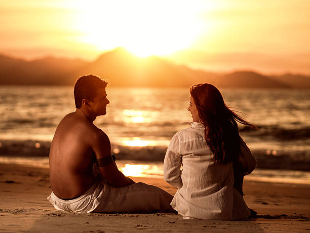 istock Young smiling couple relaxing on the beach at sunset. 487221240