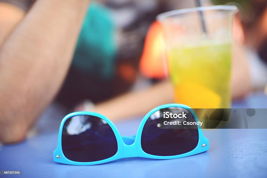 Sunglasses on the table Sunglasses on the table. Young man drinking cocktail at the background. Adult Stock Photo