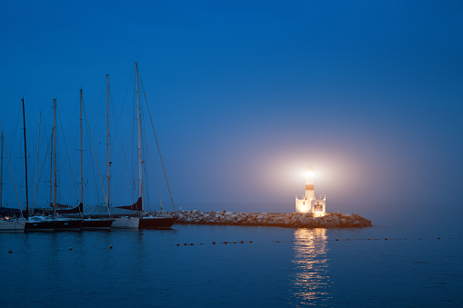 Small lighthouse shining light on a small marina with several sailing boats in Chile