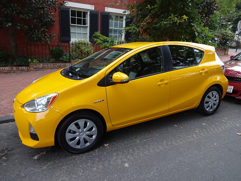 Washington DC, USA-September 4, 2015:  This yellow Toyota Prius C was spotted on a street in Georgetown of Washington DC.  The Prius C is smaller than the standard Prius and is meant to appeal to single people who do not need as much space.  Fuel economy from the 4 cylinder gas and electric powertrain is 53 city and 46 highway.