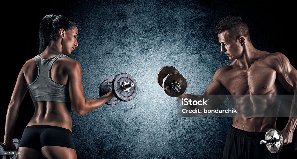 Athletic man and woman with a dumbells. Man and woman isolated on a dark background Body Building Stock Photo