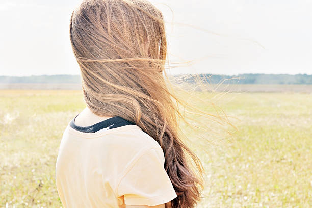 Wind flutters young girls hair who stands in the field