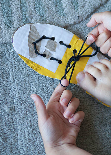 Child learning to tie shoe laces Child learning to tie shoe laces with piece of cardboard with lace through it. preschooler caucasian one person part of stock pictures, royalty-free photos & images