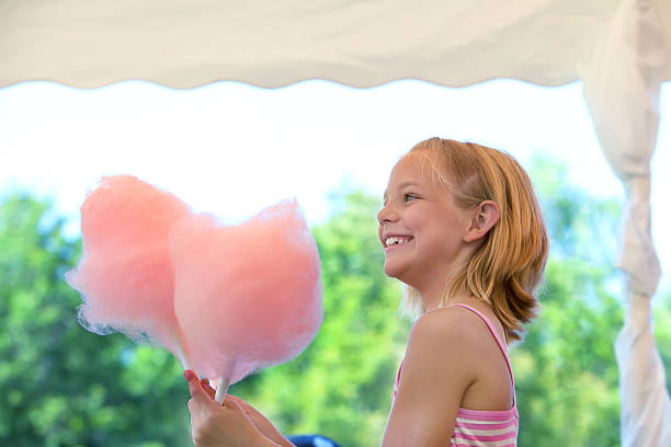 Young girl is enjoying cotton candy Cute young girl is excited about eating cotton candy.  RM child cotton candy stock pictures, royalty-free photos & images