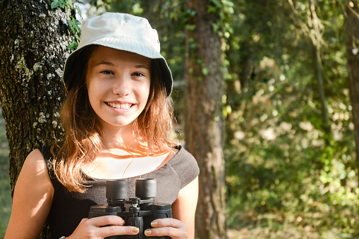 Beautiful brunette, eleven years old, holding binoculars in the forest.