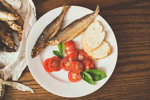 Photo of smoked fish on paper, wooden table, pepper mill