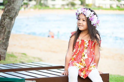 This adorable little girl is sitting on a beach chair on Poipu beach on Kawaii, Hawaii. She's on her summer vacation and has got into the Hawaiian culture/spirit by wearing a lei (flower wreath) in her hair. She's 5 years old and is Asian/Eurasian.