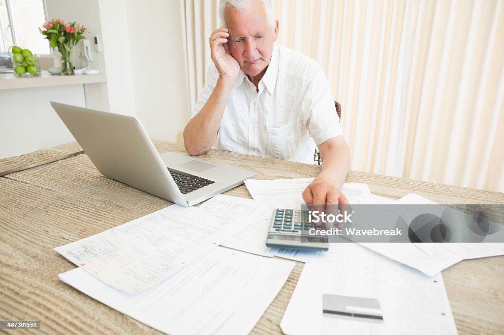 Senior man with tax documents and laptop at home Senior man being puzzled with tax documents while using laptop at home 70-79 Years Stock Photo
