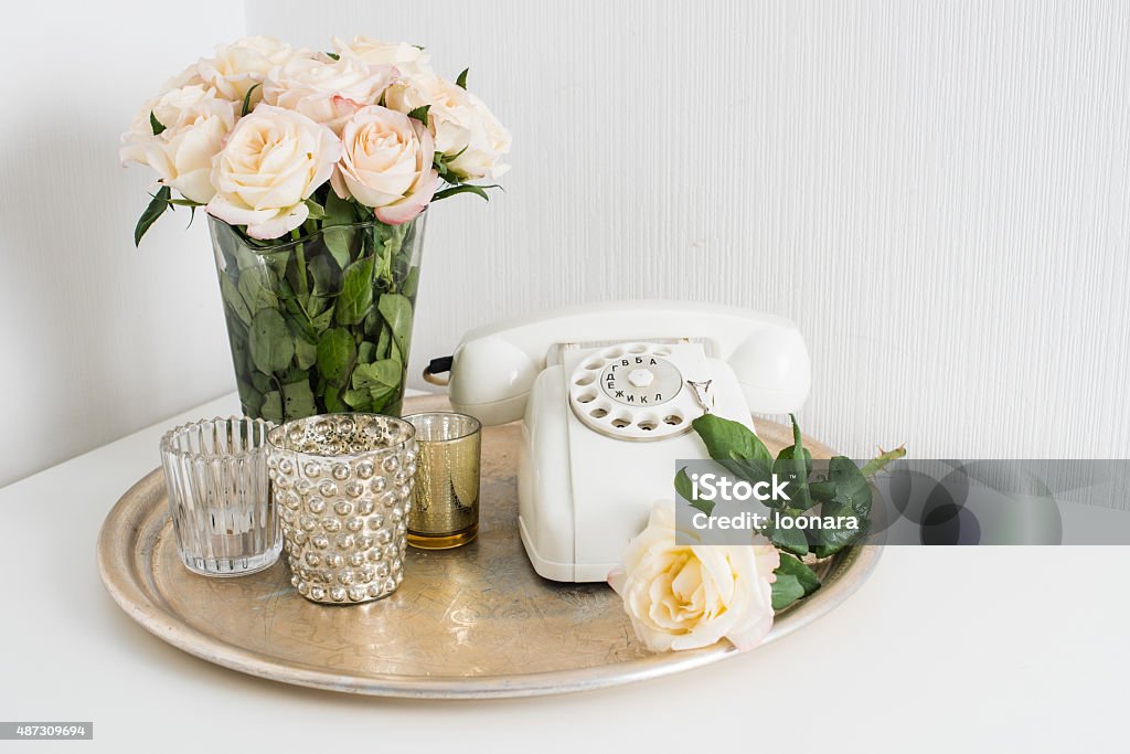 Apartment decoration retro style Vintage home interior decoration: white rotary phone, silver tray, candles and roses on a table. Apartment decoration retro style, closeup. 2015 Stock Photo