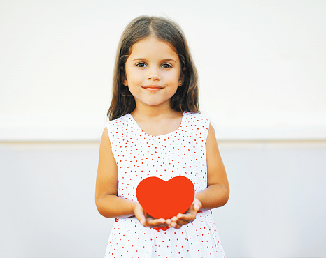 Portrait of cute little girl with red paper heart over white