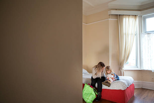 Woman's Aid A young mother and daughter sit on a bed in a dingy woman's support centre sheltering photos stock pictures, royalty-free photos & images