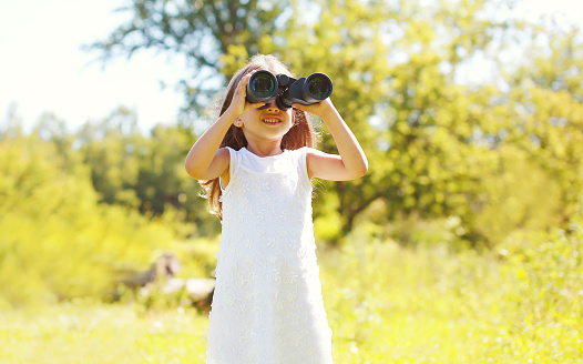Little girl child looks in binoculars outdoors in summer day