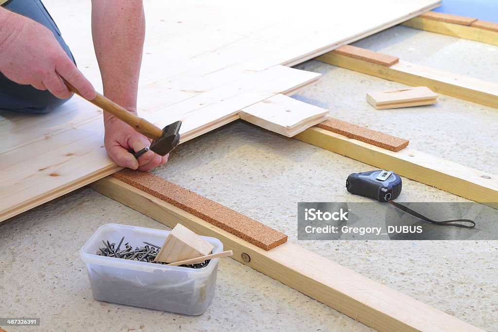 Installing parquet floor A man is installing a wooden parquet floor, nailed to wooden brackets, and with cork for noise insulation, and has all of the necessary tools. Tape measure, hammer, nails and wooden. Worker not pictured, only hands visible.  Adjusting Stock Photo