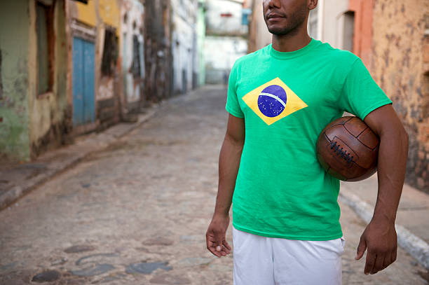 Brazilian Football Player Holding Soccer Ball Village Street Brazilian football player stands holding vintage brown soccer ball on an old rustic village street football2014 stock pictures, royalty-free photos & images