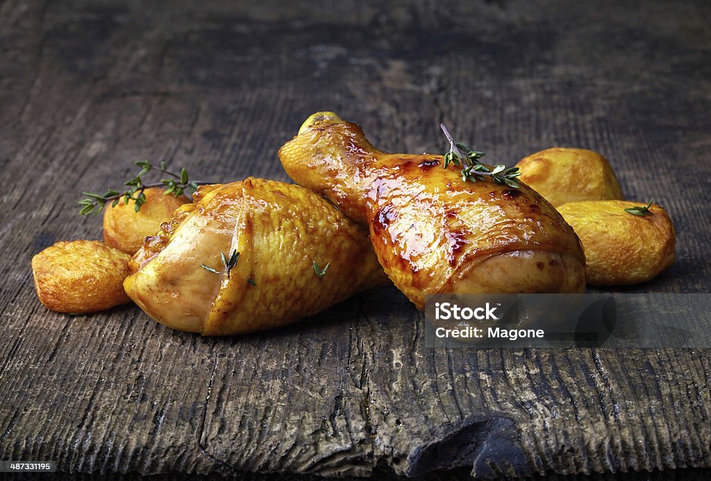 Roasted chicken legs and potatoes on wooden cutting board Baked Stock Photo