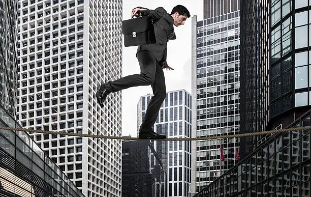 Businessman walking on tightrope against office buildings