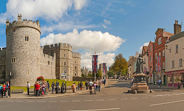 Windsor, United Kingdom - August 28, 2012: View of Windsor Castle, one of the official residences of the British Royal Family and Queen Victoria Statue with people walking and sightseeing