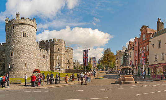Windsor, United Kingdom - August 28, 2012: View of Windsor Castle, one of the official residences of the British Royal Family and Queen Victoria Statue with people walking and sightseeing