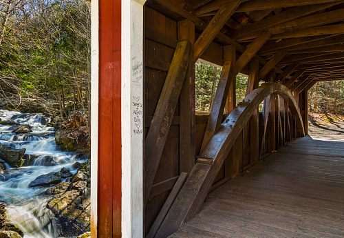 Looking through a covered bridge which sits above eight-mile brook flowing heavily after a hard rain in early spring.