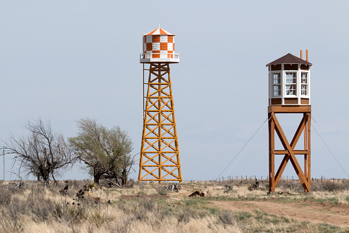 A World War Two era cement foundation of barracks stands in the foreground as a reconstructed guard house and water tower stand behind on the plains of southeast Colorado at the Amache Japanese-American Relocation Center. 