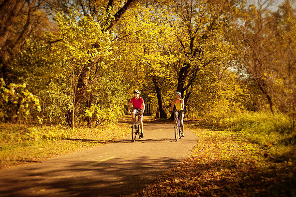 Two bicyclists bicycling on a park bike path in Autumn color. Young Caucasian man and a black American young woman exercising together in a nature park together. Photographed on location in Minneapolis,f Minnesota, USA in horizontal format with available copy space.
