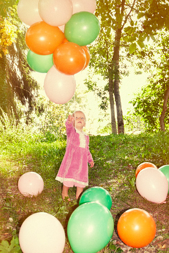 Cute little girl holding a bunch of balloons in the park