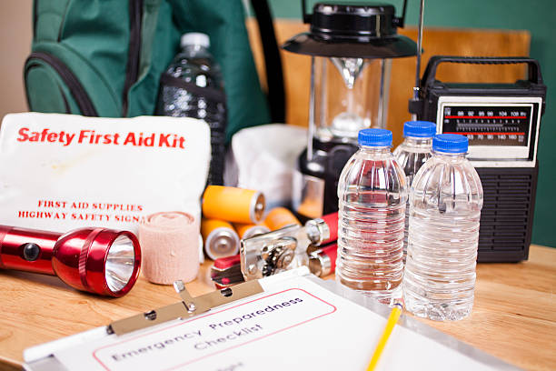 Emergency preparedness checklist and natural disaster supplies. Emergency preparedness checklist on clipboard with pencil and a large pile of supplies to be used in case of a natural disaster (hurricane, flood, earthquake, etc.) including: flashlight, batteries, water bottles, first aid kit, lantern, radio, mask.  No people. first aid photos stock pictures, royalty-free photos & images