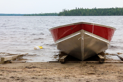 Image of an aluminum red and silver colored fishing boat with a yellow minnow container parked on the beach.  Smoothrock lake is in northern Ontario in Canada.  It is a remote lake, known for fly in fishing and canoeing.