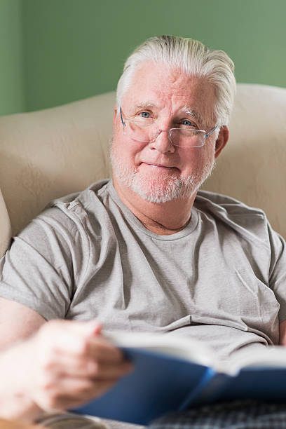 istock Senior man in living room reading book 487379652