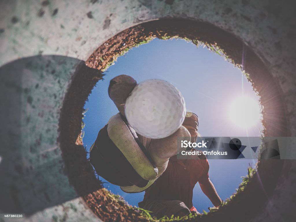 Point Of View Golf Player and Ball From Inside Hole A Point Of View picture of a Golf Player picking up a Golf Ball view From Inside the Hole on a sunny day of summer. Golf Stock Photo