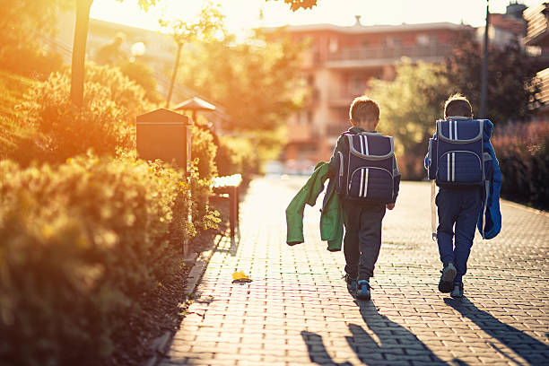 Two little boys returning from school Two little boys wearing blue backpacks or schoolbags walking in residential area walkway. Little brothers are either going to school in the morning or returning from school in the evening. satchel stock pictures, royalty-free photos & images