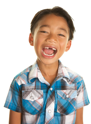 A handsome Filipino Boy on a white background.  He is looking at the camera with a big open mouth smile.  You can see that he is missing his two front teeth. He is wearing a short sleeved plaid shirt.