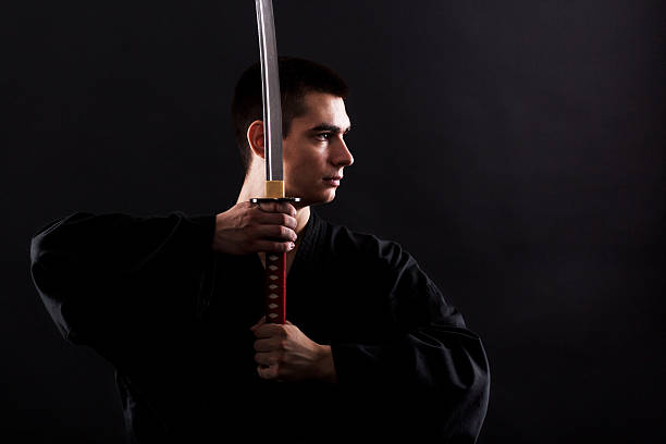 Young martial arts fighter with katana on black background