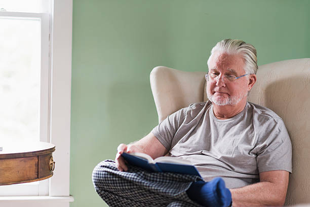 istock Senior man in living room reading book 487391262