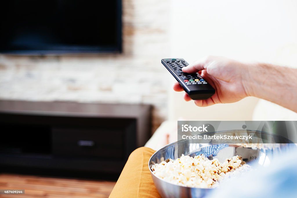 What channel is it on? Close-up of a hand holding a remote control and a bowl of popcorn Movie Stock Photo