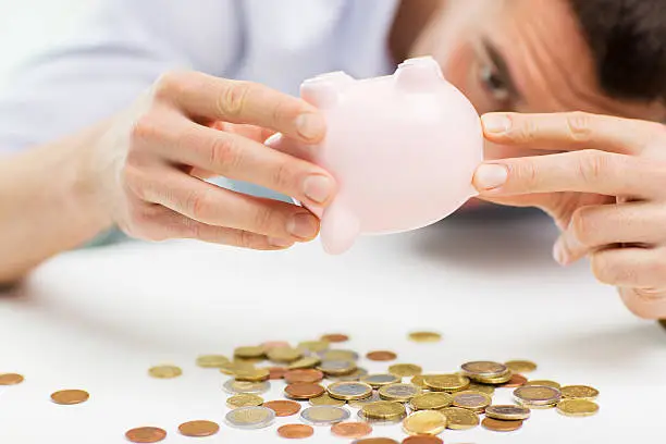 Photo of close up of man pouring coins from piggy bank