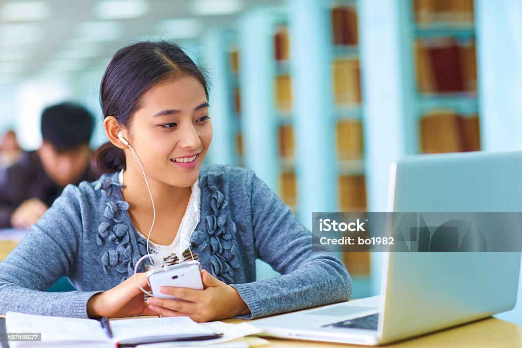 pretty asian college student in the library one pretty young asian college student using smartphone and laptop in the library 20-24 Years Stock Photo