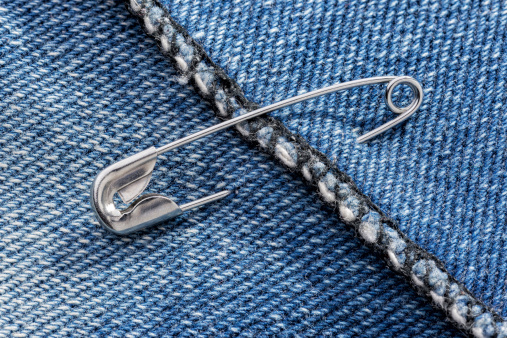 Closed safety pins on a blue jeans denim fabric