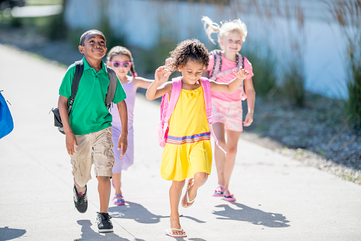 A multi-ethnic group of elementary age children are skipping and running outside class on their way to school.