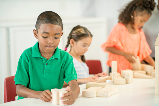 A multi-ethnic group of elementary age children are sitting at the table and playing with a bunch of wood blocks.