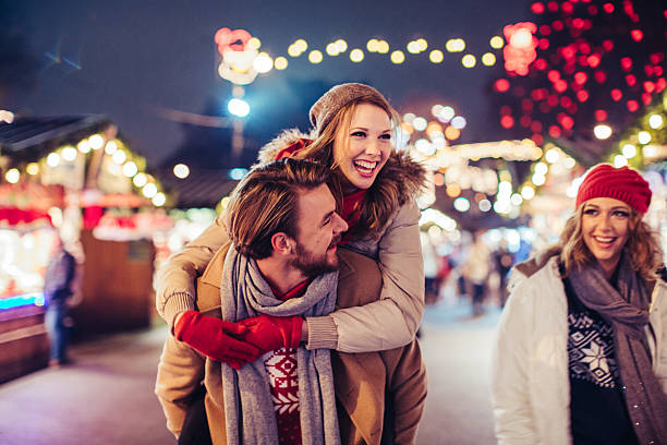 Couple having fun outdoors at winter fair. Young couple having fun outdoors at winter fair. Wearing warm clothes, hats and scarfs. Visiting christmas market in Vienna, Austria. Everything is decorated with festive string lights. Evening or night with beautiful lights lightning the scenes. holidays and celebrations stock pictures, royalty-free photos & images