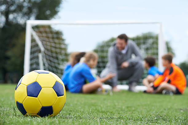 Coach  And Team Discussing Soccer Tactics With Ball In Foregroun Coach  And Team Discussing Soccer Tactics With Ball In Foreground high school student child little boys junior high stock pictures, royalty-free photos & images