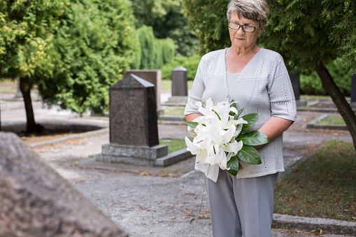 Photo of mature woman on cemetery holding white lilies