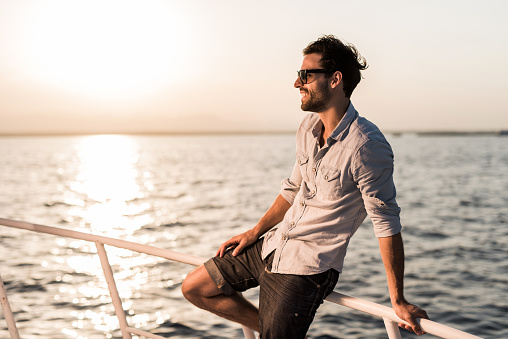 Smiling man traveling on boat and enjoying in summer day at sunset. Copy space.