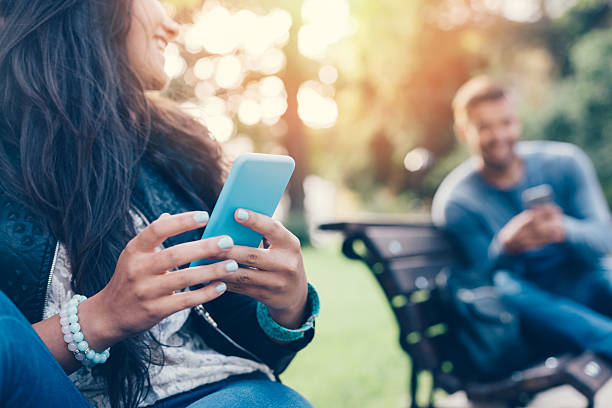 flirting couple in the park texting on smartphones - 網路約會 個照片及圖片檔