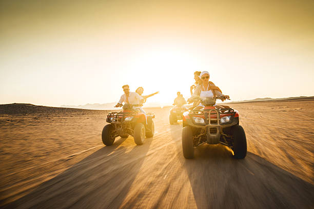 jeunes amis s'amusant sur quatre vélos au coucher du soleil. - off road vehicle quadbike desert dirt road photos et images de collection