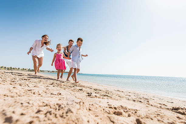 молодые игривый семья, преследуя на пляже в летнее время. - family fun running couple стоковые фото и изображения