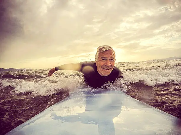 Very active senior man, surfing on a wave with a surfboard