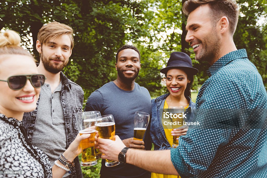 Multi ethnic friends drinking beer in the park Multi ethnic group of happy friends - caucasian and afro american - toasting with beer glasses outdoors.  Celebratory Toast Stock Photo