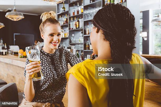 Two Young Women Talking In A Pub Stock Photo - Download Image Now - After Work, Alcohol - Drink, Bar - Drink Establishment